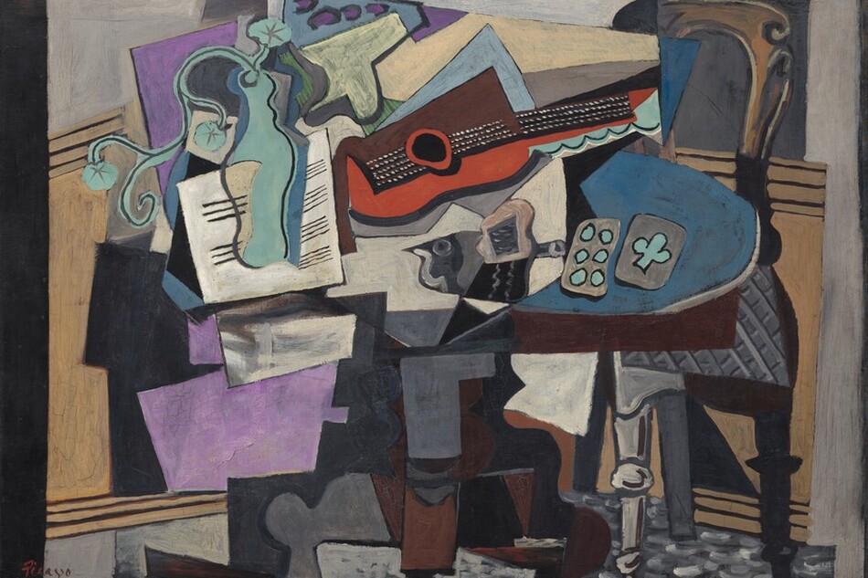Abstracted objects, including a guitar, vase, papers, and playing cards, are gathered on a tabletop in this horizontal still life painting. The objects are made up of areas of mostly flat color and many are outlined in black, creating the impression that the some shapes are two-dimensional and assembled almost like a collage. The brown table has an oval top and a curving pedestal foot. At the center of the jumble on the tabletop, a guitar lies on its side with the neck facing us and reaching to our right. Beneath the black fretboard and neck, the curving form of the guitar is painted tomato red. The upper half is represented by a squared-off brown form. The guitar seems to rest atop or in front of an array of stacked shapes, like splayed pieces of paper, in white, lavender purple, and pale blue. A curving form painted in turquoise to our left seems to be a vase holding a spray of three flowers. The vase is shown against a white square painted with horizontal black lines, like sheet music. A dark gray form at the middle of the table, beneath the guitar, could be the silhouette of a bird facing our left. Just to the right of the bird, a pair of playing cards lie on a blue area. Painted in turquoise against gray, one card has six dots and the other one club. A chair with a curved, arching top and a gray upholstered seat is pulled up to the table to our right. The front left leg is light gray with turned knobs near the foot and halfway up the leg; the right leg is painted black, as if in shadow. Panels of pale tan suggest wainscotting behind the table beneath a pale gray wall across the background. The overall impression of the painting is fragmented as even single objects seem to be broken up into planes and areas of color. The artist signed and underlined his name with red paint in the lower left corner: “Picasso.”