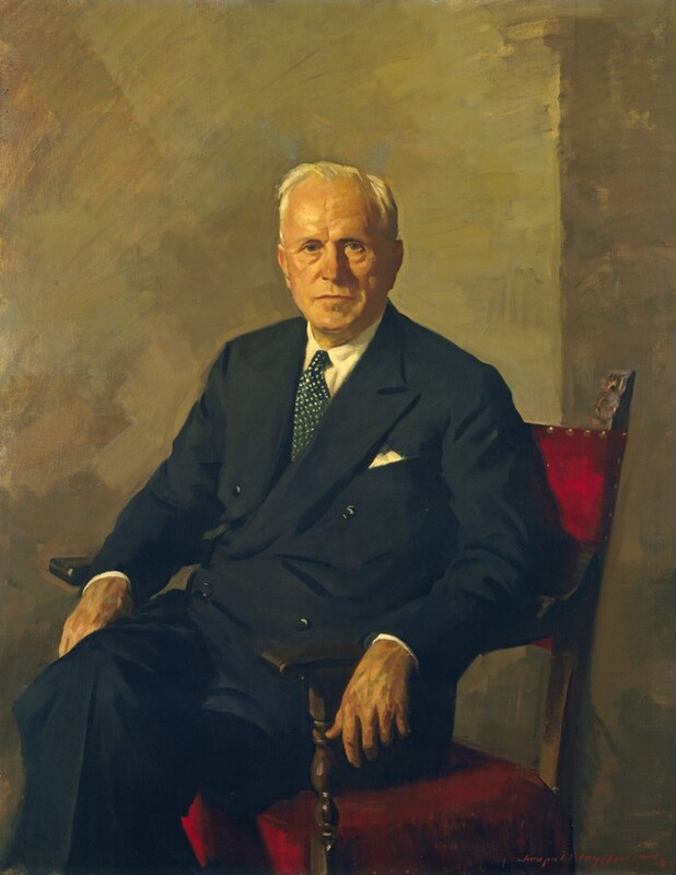 Shown from the shins up, a pale-skinned, cleanshaven man wearing a black suit sits and looks out at us in this vertical portrait painting. His legs are crossed and knees angled to our left, but he turns his face to us. He has a round face with slight bags under his gray eyes, and his thin lips are closed. His cheeks and jowls are a bit fleshy with age, and short white hair is brushed back from his high forehead. He wears a double-breasted jacket over a white shirt and dark blue tie with white polka dots. A white pocket square peeks out of the breast pocket. Both of the man’s elbows rest along the wood arms of his chair, which is upholstered on the back and seat with ruby-red fabric. The supports under the arms are turned, and top of the vertical style holding up the backrest that we can see is carved. The chair is near the corner of a room with walls painted muted sage green and tan. Brushstrokes are visible throughout and are especially loose in the background. The artist signed and dated the canvas with red paint in the lower right corner, “Leopold Seyffert 53.”
