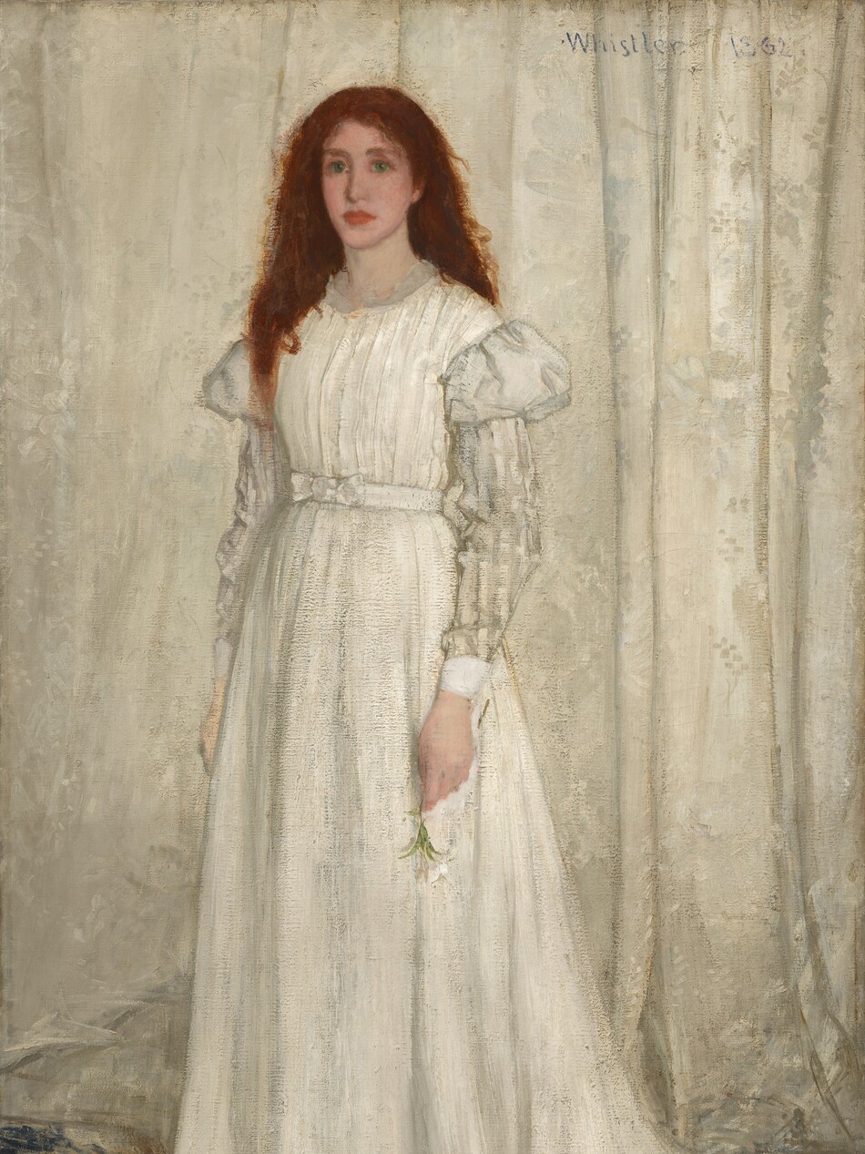A young woman with pale, peachy skin, wearing a long, flowing white dress, stands in front of a white curtain in this vertical portrait painting. Her auburn-red hair cascades down over and behind her shoulders. She looks to our left with green eyes, and her pink, full lips are closed. Her dress has puffed shoulders above a white-on-white striped pattern on the long sleeves. She stands on an animal pelt; it is not clear whether it is a wolf or a bear. The pelt spans the width of the painting and overlaps a blue patterned carpet. The animal’s mouth gapes to show sharp teeth. Its glassy eyes are wide open, and it seems to look at us. The edges of the animal skin are red. The woman holds a white lily by her side in her left hand, while yellow and purple flowers lie scattered on the pelt.