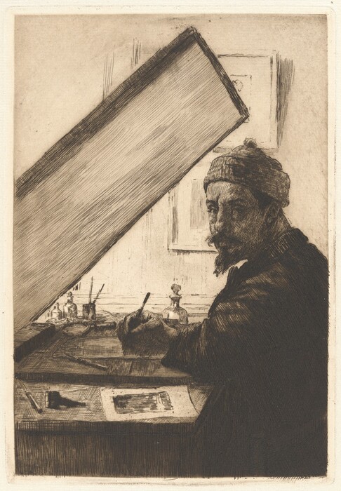 The image shows a man sitting at a desk with various objects like bottles, a palette, and brushes in front of him. He wears a knitted cap and a dark robe. He is holding a writing instrument over a piece of paper, with a framed picture partially visible in the background.