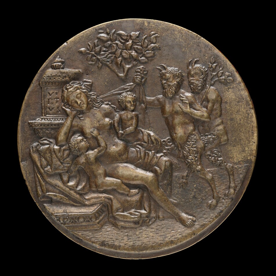 The sculpture depicts a reclining female figure with flowing drapery, resting against an elaborate architectural element resembling an altar or pedestal. Beside her is a youthful figure, while another young figure looks upon her with an arm raised. On the right side, two satyr-like figures engage in interaction, one holding a cloth. Above, a tree with leafy branches is present. The material is metallic, likely bronze, with a dark brown surface and areas of patina. The sculpture is circular and showcases intricate detail.