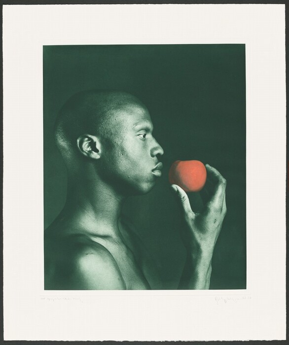 The image shows a person from the shoulders up in a side profile. The person is upright, holding an apple near their face with their right hand. The person has a shaved head and distinct facial features, including a straight nose and full lips. They are not wearing any clothing or accessories that are visible from this angle. The background is a solid dark green.