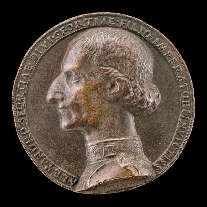 The sculpture is a medallion featuring the profile view of a man's head. The man is depicted with detailed facial features and short, wavy hair. The medallion is made of metal with a muted silver or bronze color. Surrounding the profile, there is an inscribed text along the outer edges of the medallion. The man is shown wearing a garment with a patterned texture around the neck resembling a high collar. The sculpture is intricately crafted, with fine attention to detail in the hair and facial characteristics, giving it a lifelike yet stylized appearance.