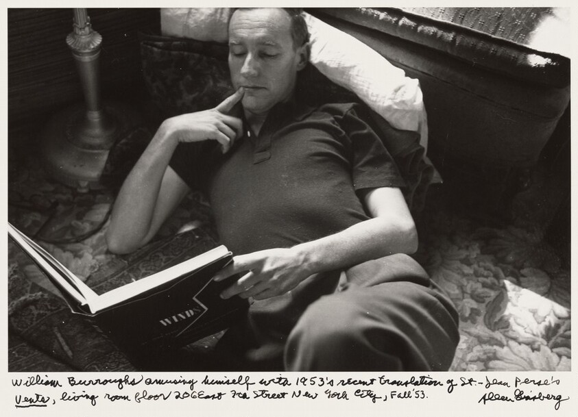 William Burroughs amusing himself with 1953's recent translation of St.-Jean Perse's _Vents_, living room floor 206 East 7th Street New York City, Fall '53.