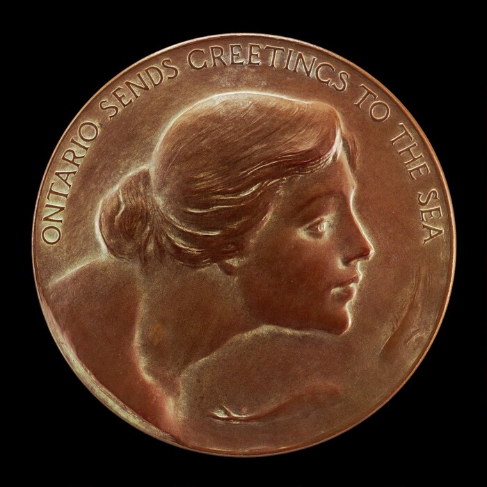 The sculpture depicted on this circular bronze medallion is a woman's profile. The woman has a calm and serene expression, her hair styled in a neat bun at the back of her head. The material of the sculpture is bronze, giving it a metallic brown color with a subtle sheen. The lettering around the edge of the medallion reads "ONTARIO SENDS GREETINGS TO THE SEA." The sculpture is a raised relief, with the woman's face and text elevated above the background of the medallion.