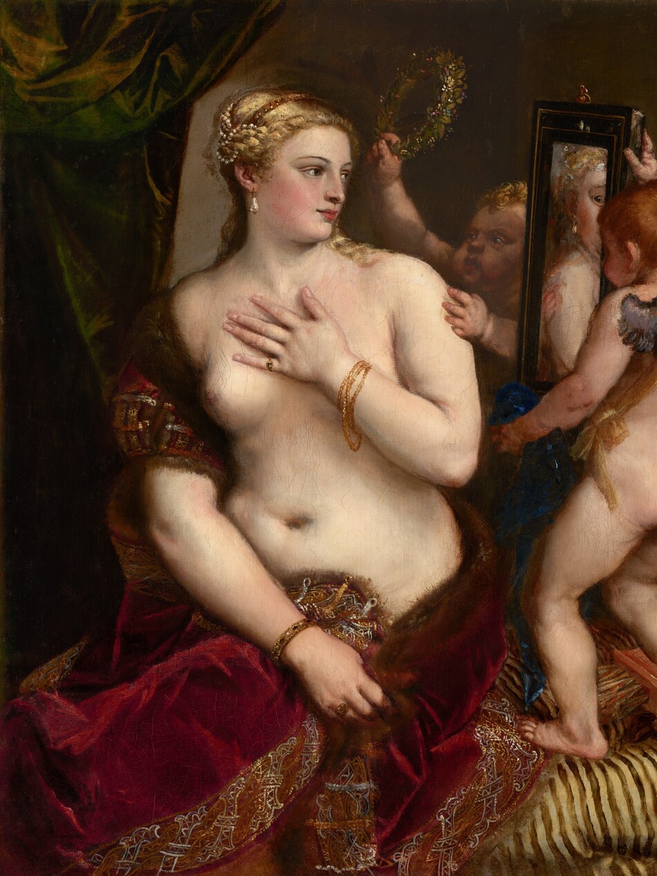 A partially nude woman with pale, peachy skin sits to our left looking into a mirror held up by a nearly nude, winged child to our right in this vertical painting. The woman’s body is angled to our left but she looks across her body to our right. She holds her left hand to her chest, and her right hand grips the fur-lined edge of the scarlet-red, velvet fabric that drapes over that upper arm and around her hips. Her blond hair is coiled up in rows of pearls, and she has dark eyes, a straight nose, and her pale pink lips turn up in a subtle smile. A teardrop pearl earring hangs from the ear we can see, and she wears rings and gold bracelets. The child-like figure to the right stands on a gold-striped cushion facing away from us as he holds up the rectangular, black-framed mirror. He has small silver wings and a sash of golden yellow hangs from one shoulder around the opposite hip. A second child reaches from behind the mirror to hold up a ring of laurel leaves. A forest-green curtain is gathered in the upper left corner and the beige wall beyond falls into shadow to our right.