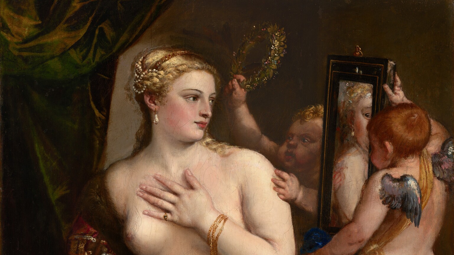 A partially nude woman with pale, peachy skin sits to our left looking into a mirror held up by a nearly nude, winged child to our right in this vertical painting. The woman’s body is angled to our left but she looks across her body to our right. She holds her left hand to her chest, and her right hand grips the fur-lined edge of the scarlet-red, velvet fabric that drapes over that upper arm and around her hips. Her blond hair is coiled up in rows of pearls, and she has dark eyes, a straight nose, and her pale pink lips turn up in a subtle smile. A teardrop pearl earring hangs from the ear we can see, and she wears rings and gold bracelets. The child-like figure to the right stands on a gold-striped cushion facing away from us as he holds up the rectangular, black-framed mirror. He has small silver wings and a sash of golden yellow hangs from one shoulder around the opposite hip. A second child reaches from behind the mirror to hold up a ring of laurel leaves. A forest-green curtain is gathered in the upper left corner and the beige wall beyond falls into shadow to our right.