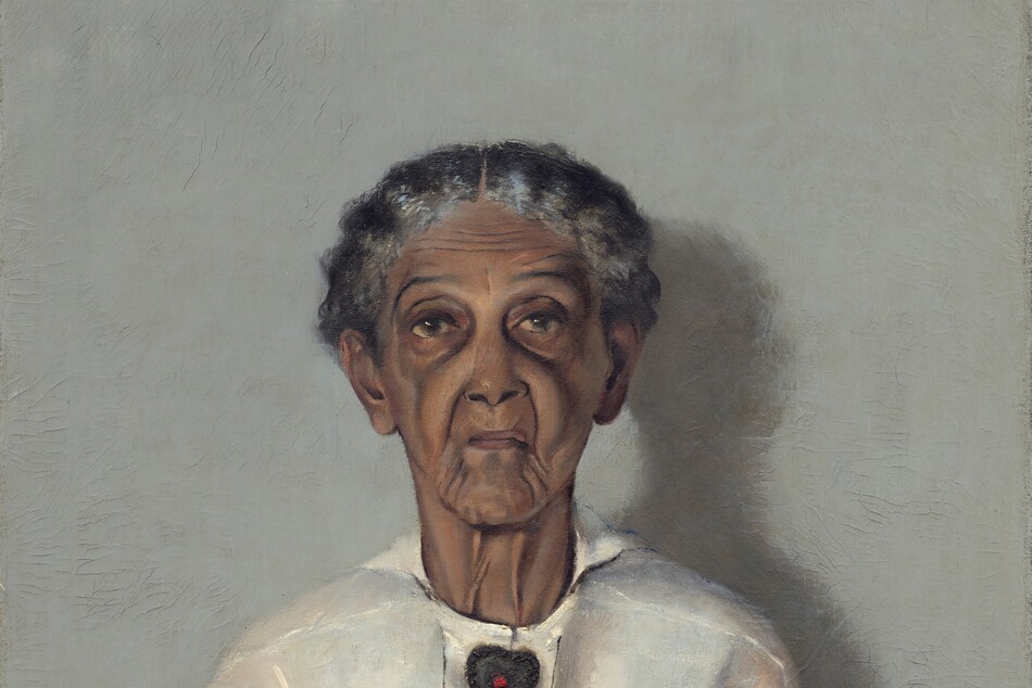 Shown from the knees up, a woman with brown, wrinkled skin, wearing a white blouse, apron, and black skirt is shown in front of a pale gray background in this vertical portrait painting. Straight-backed, she faces and looks at us with her hands resting in her lap. Her wavy, iron-gray hair is parted in the center and pulled back from her face. Her eyebrows are slightly raised, and her face is deeply lined down her cheeks and around her mouth. She wears a heart-shaped brooch with a red stone at its center at her neck and a gold band on her left ring finger. The light coming from our left casts a shadow against the wall to our right. The artist signed and dated the painting in the lower right corner: “A.J. MOTLEY. JR. 1922.”