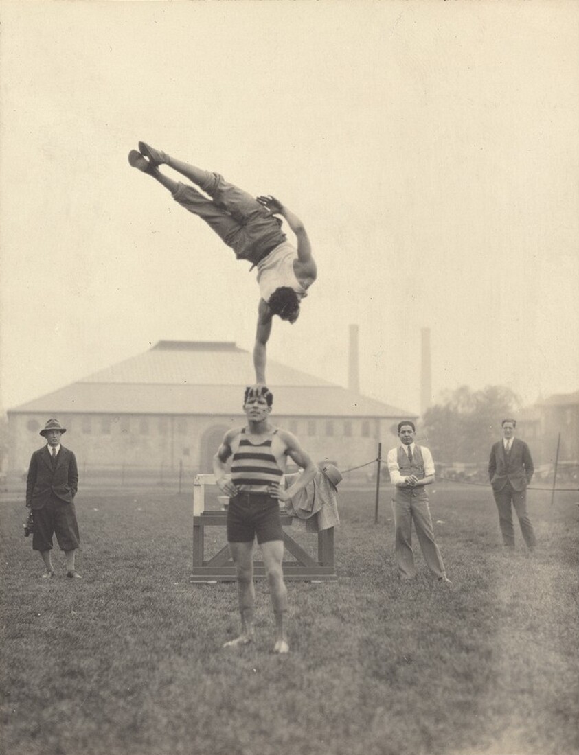 Untitled (Man balanced in one-armed handstand on top of another man's head)