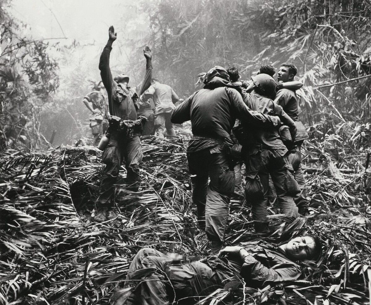 Paratroopers aid wounded comrades as one GI guides a medical evacuation helicopter into a jungle clearing