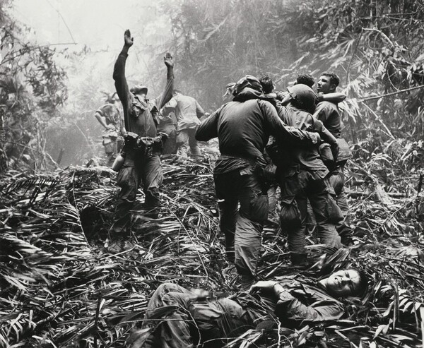 Paratroopers aid wounded comrades as one GI guides a medical evacuation helicopter into a jungle clearing