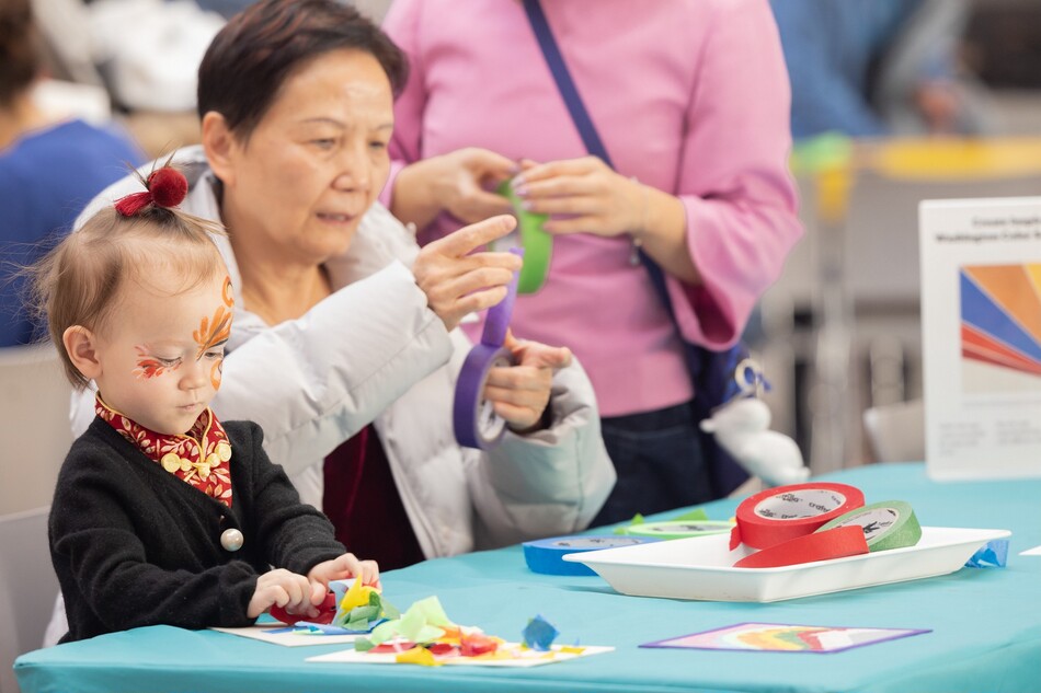 A little girl sitting at a table next to two women and all are working on arts and crafts projects.