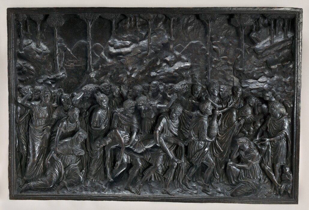 Two men carry a dead body amid a crowd of about thirty people in this rectangular, horizontal panel, which is cast in low and high relief. The dead man’s limp body is carried by one person who supports his knees and legs and the other his torso. The closely knit crowd is made of men and women, who all wear voluminous robes that fall in lively, pleated folds. The group moves to the right, where a woman kneels with one hand held to forehead. Some people swing their arms wide or hold their hands to their heads, crying. A few children are in or near the cave opening to the right. A rocky landscape with spindly trees presses close behind them.
