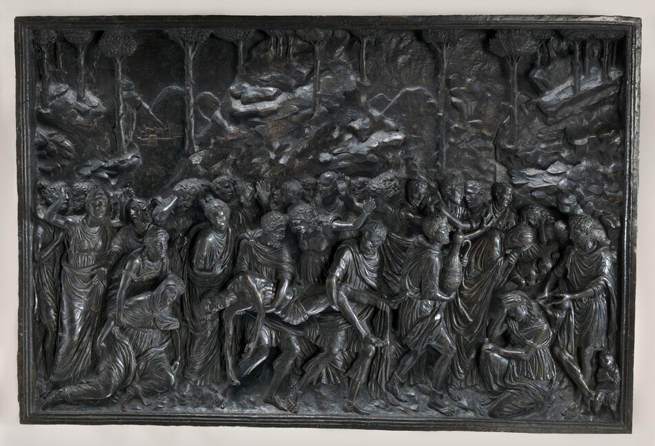 Two men carry a dead body amid a crowd of about thirty people in this rectangular, horizontal panel, which is cast in low and high relief. The dead man’s limp body is carried by one person who supports his knees and legs and the other his torso. The closely knit crowd is made of men and women, who all wear voluminous robes that fall in lively, pleated folds. The group moves to the right, where a woman kneels with one hand held to forehead. Some people swing their arms wide or hold their hands to their heads, crying. A few children are in or near the cave opening to the right. A rocky landscape with spindly trees presses close behind them.