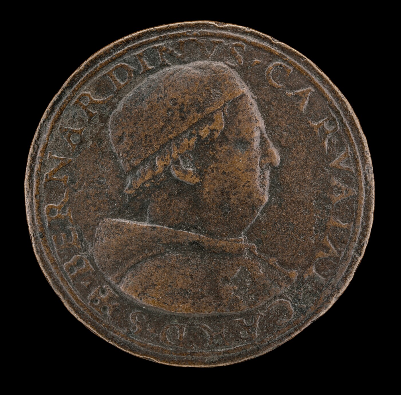 The image shows a round sculpture shaped like a medal or coin, with a profile portrait of a man facing right. The figure is wearing a textured cap and a garment that wraps around the shoulder. The material appears to be metal, possibly bronze, with a dark brownish patina. The surface shows signs of age with spots and a slightly worn texture. Around the profile are inscriptions in a circular pattern along the edge of the coin. The sculpture is flat, emphasizing the relief detail of the portrait and text, which is typical of a coin-like sculpture.