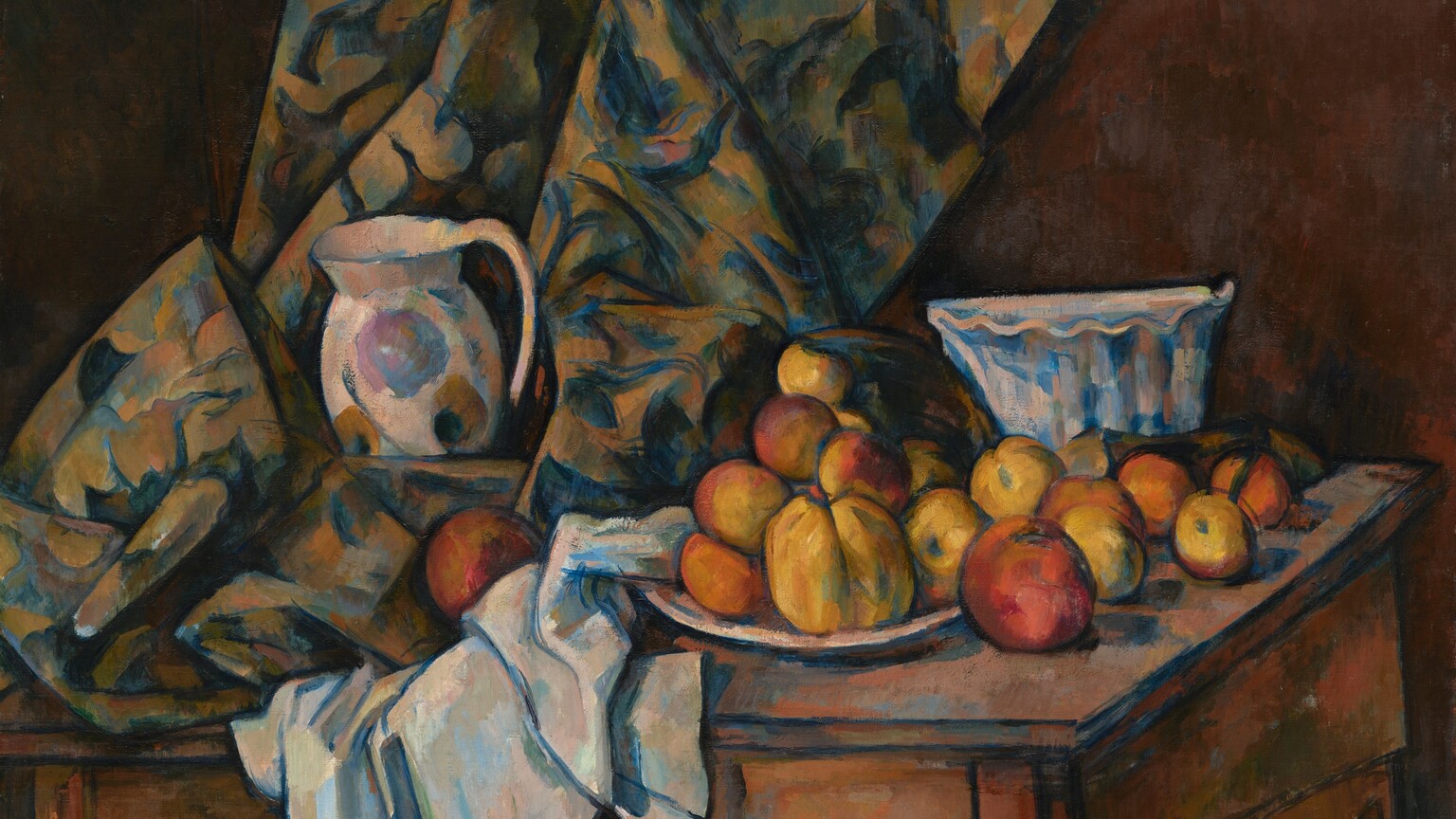 About a dozen rust-orange and golden yellow apples and peaches are arranged on a white plate next to white and floral-patterned cloths nestled around a white pitcher and bowl, all on a wood tabletop that tilts toward us in this nearly square still life painting. A curtain patterned with royal blue, olive green, and beige falls along or near the back wall of the room and rests on the table to our left. The white pitcher is painted loosely with the suggestion of harvest-gold and pale lilac-purple flowers, and it sits amid the pooling folds of the curtain to our left. The white tablecloth is bunched under and next to it to our right, at the middle of the composition. The fruit is arranged on and around a white plate next to the tablecloth. A tall bowl with fluted sides and a ruffled, scalloped rim sits behind the fruit, near the right edge of the table. The curving skirt of the table reaches nearly to the bottom edge of the canvas. All the objects in the painting are outlined with dark blue and the shadows are painted with patches of spruce and cobalt blue.