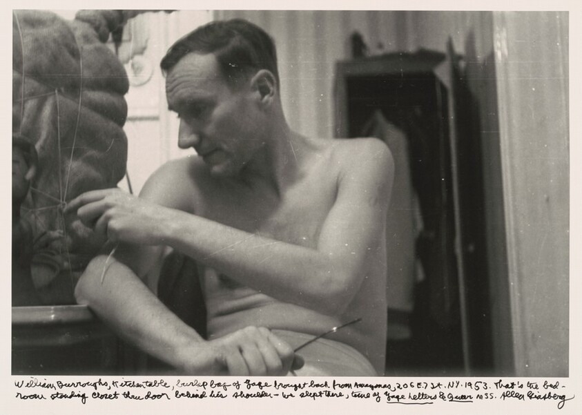William Burroughs, kitchen table, burlap bag of Yage brought back from Amazonas, 206 E. 7 St. NY. 1953. That's the bedroom standing closet through door behind his shoulder-- we slept there, time of _Yage Letters_ & _Queer_ mss.