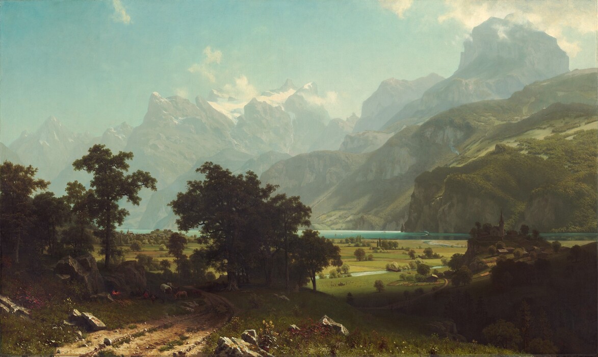 From a little above a dirt road, we look past a grove of trees to a broad plain and a lake at the foot of towering, hazy mountains in this horizontal landscape painting. The narrow, teal-blue lake runs from left to right along the horizon, which comes about a third of the way up the composition so the hills and mountains take up most of the picture. On the far shore of the lake, steep hills are thick with fern-green trees and growth. Beyond these hills, muted gray and green rocky mountains reach precipitously into the clear, robin’s egg-blue sky so some nearly touch the top edge of the canvas. Snow nestles in the mountain peaks while gauzy mist hovers among the mountain tops. The meadow below is a patchwork of avocado-green and sand-brown fields. An ice-blue stream winds from the lake across the plain while olive-green trees and shrubs dot the fields. Closest to us, in the lower left corner of the painting, small stones and clumps of green grass run along the dirt road, and boulders line it to either side. A band of dark green spanning the road creates a screen a short distance from us, in the lower left quadrant of the composition. Through the trees is a view of minuscule buildings lining the lakeside. In the shadows, under the trees, people camp with a covered wagon covered in white fabric and several animals including a donkey. A red and yellow fire glows, almost lost in the deep shadows of the trees, next to the people. On our right, about a dozen people with a horse-drawn wagon, all tiny in scale, work in the field next to the stream. Farther along the stream, another wagon approaches a covered bridge. On our right and close to us, a dark shadow falls across the landscape. Beyond the shadow, a group of buildings with a church in the center sit on a low hill.