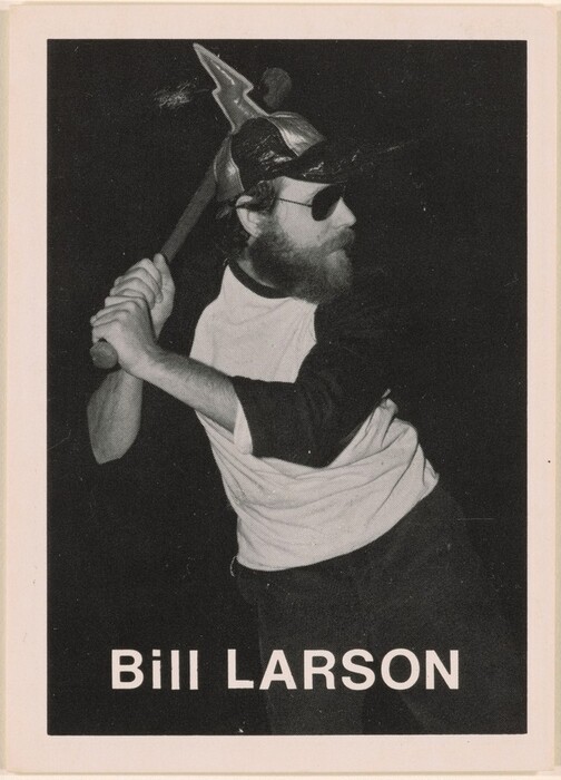 The image depicts a man standing with a large hammer held over his right shoulder. He has a full beard, wears glasses, and a cap with large, pointed details. He is wearing a long-sleeve shirt with dark sleeves and a lighter body. The background is dark with white text below reading "Bill Larson."