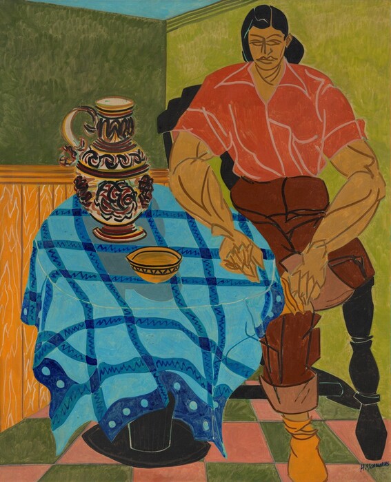 The image depicts a person seated at a table. The individual has strong facial features including a prominent jawline and a straight nose. They have dark, sleek hair styled in a slicked-back manner, and are wearing a red collared shirt tucked into brown pants. The table in front of them is covered with a vibrant blue cloth featuring an intricate design, with a patterned jug and a small bowl on top. The background consists of a divided wall with a green upper section and a wood-textured lower section, alongside a pink and green checkered floor.