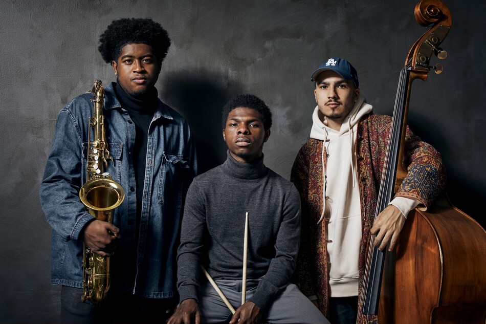 A band, made up of three young men, holding their instruments.