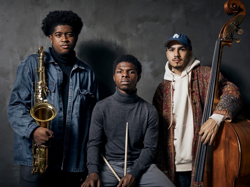 A band, made up of three young men, holding their instruments.