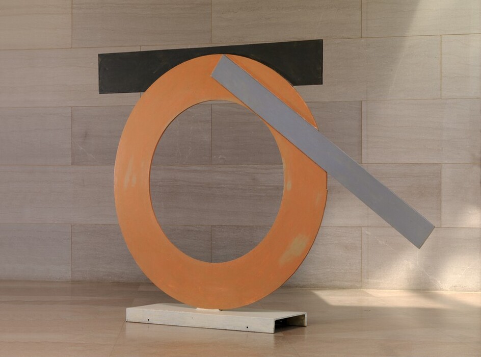 Made with sheets of painted steel, an orange ring stands upright on a narrow white base in this freestanding sculpture. A black strip and a gray strip are affixed to the edges of the ring. The black strip is horizontal across the top of the circle, attached to the back side of the ring, and the narrower but longer gray strip is angled across the top right quarter of the circle. The sculpture is photographed near a wall clad with pale pinkish-gray marble and a similarly colored floor.