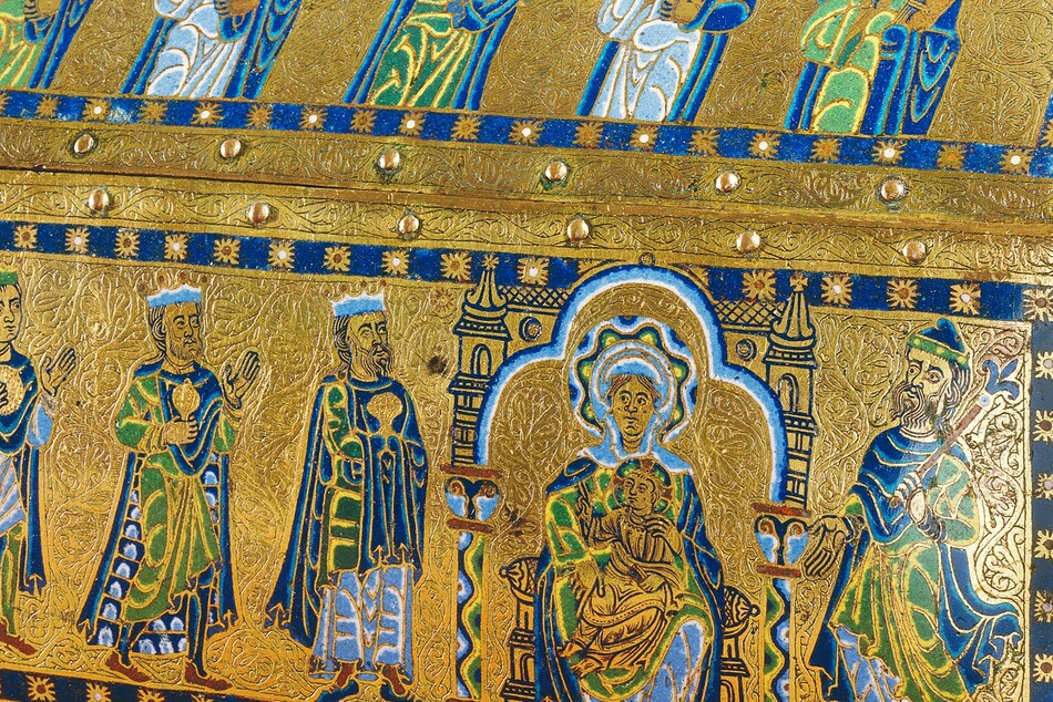 A free-standing, gold, enameled, rectangular box has a triangular top like the roof of a house, and the box rests on a short, square foot in each corner. In this photograph, we look onto one long side and the short side to our right is angled toward us, so we see the panel there, too. Along the long side, five people are shown from the waist up in the upper, roof-like panel and six more line up on the panel below. The skin of every person is gold, and all wear robes and garments in lapis or sky blue, spring green, yellow, and white. The area around the people is also gold, and each panel is encased by a royal-blue band dotted with stylized stars at regular intervals. Each panel is then lined with small, button-like rounded bosses around its edges. In the upper panel, all of the men except the second from the right have beards, and all have halos with wavy bands of blue, green, yellow, and white. The man to our left holds a book and his neighbor a skeleton key the length of his arm. The man at the center holds up a book with his left hand, on our right, and raises the index and middle fingers of his other hand, held up at shoulder height. The two men to our right also hold books. In the panel below, three horses’ heads peek in from the left edge, creating a vertical band, and three crowned men line up, holding gold vessels and looking toward a woman seated in a throne with a child on her lap. The woman has a halo made with a wavy pattern of blue, yellow, green, black, and white. Her throne is flanked by columns, and the area around it is edged with bands of white, light, and dark blue. The baby wears gold, has a halo, holds a book in his lap with his left hand, and raises the first two fingers of his other hand toward the three men. The final person in this panel wears a hat, holds a scepter topped with a fleur-de-lis, and gestures at the woman and baby. The head and shoulders of a haloed person is visible along the short side of the box, which is angled sharply away from us. The gold between all the people and bordering each panel is intricately carved with tiny flowing organic lines and swirls.