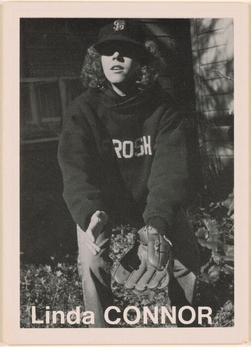 The image shows a person in a crouched position with arms outstretched forward. They have curly hair, a cap with "SF" on it, a shadowed face, a long-sleeved sweatshirt with "ROSH" visible, and a baseball glove on one hand. The background includes foliage, a blurred building, and is monochrome. The text "Linda CONNOR" is printed at the bottom.