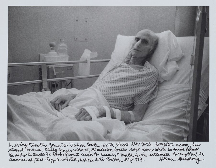 An emaciated, bald man lies propped up in a hospital bed in this horizontally oriented black and white photograph. His body is to our left, and he turns to look at us, propped on a pillow on the raised head of the bed. His eyes are sunken, and his hands are curled in loose claws. He wears a polka-dotted hospital gown, and his lower body is covered by a crumpled white sheet. His arms lie on the sheet with rows of white tape holding tubes in place and a long tube runs into his nose. An IV pole with a plastic tube hanging from it extends the height of the image near the right edge, while a cart holding a bottle and another object with a bulbous top stands by to the wall beyond his bed. A white jug is hooked over the bed railing on that side. The artist has written in script underneath the image, “Living Theater genius Julian Beck 48th Street New York hospital room, his stomach-abdomen lining cancer allowed remission for the next year while he made films & video & theater & books from Zurich to Miami; ‘Death is the ultimate corruption,’ he announced, that day I visited, Medical Arts Center, May 1984. Allen Ginsberg.”