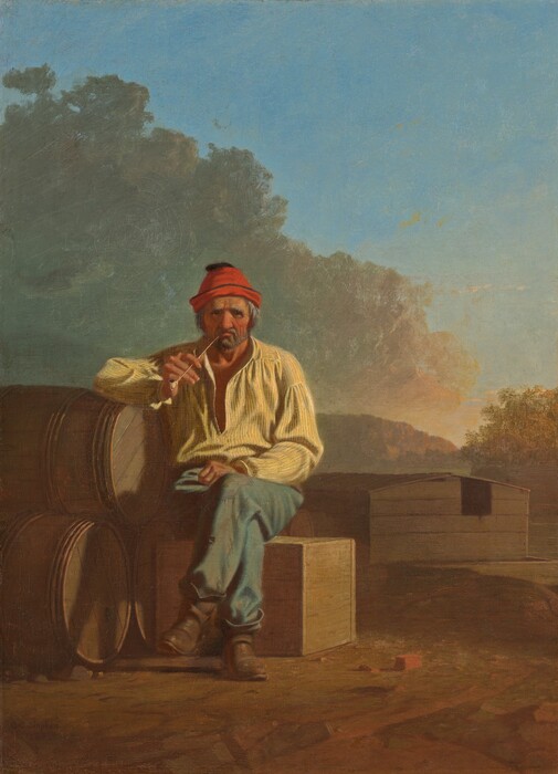 A bearded man with wrinkled, peachy skin and reddened cheeks sits and smokes a pipe on a wooden box in a landscape in this vertical painting. The man’s body faces us, and he peers at us with dark eyes under heavy, bushy white brows. Wrinkles line his forehead, the corners of his eyes, and his cheeks. He has a bulbous nose and a gray beard, and the long-stem pipe is pinched in his downturned mouth. His shaggy gray hair is covered by a cardinal-red cap. He wears a blousy daffodil-yellow shirt, which is loose around the neck, faded and patched blue pants, and scuffed brown boots. His legs are crossed with one knee over the other, and one fist rests in his lap. The other elbow is propped on a pyramid of three wooden barrels stacked on their sides to our left. A few bits of bricks or red stones are near the man’s feet, and a wooden houseboat with a low-pitched roof is in the near distance, to our right. The platform under the structure floats on a river, which is lined with trees to our right and mountains to our left. The sunset warms the face of the mountains and the trees to red and gold. Sage-green and peach clouds billow above the man, dividing the sky diagonally in front of bright blue sky beyond. The artist signed and dated the painting in the lower left corner, “G.C. Bingham 1850.”