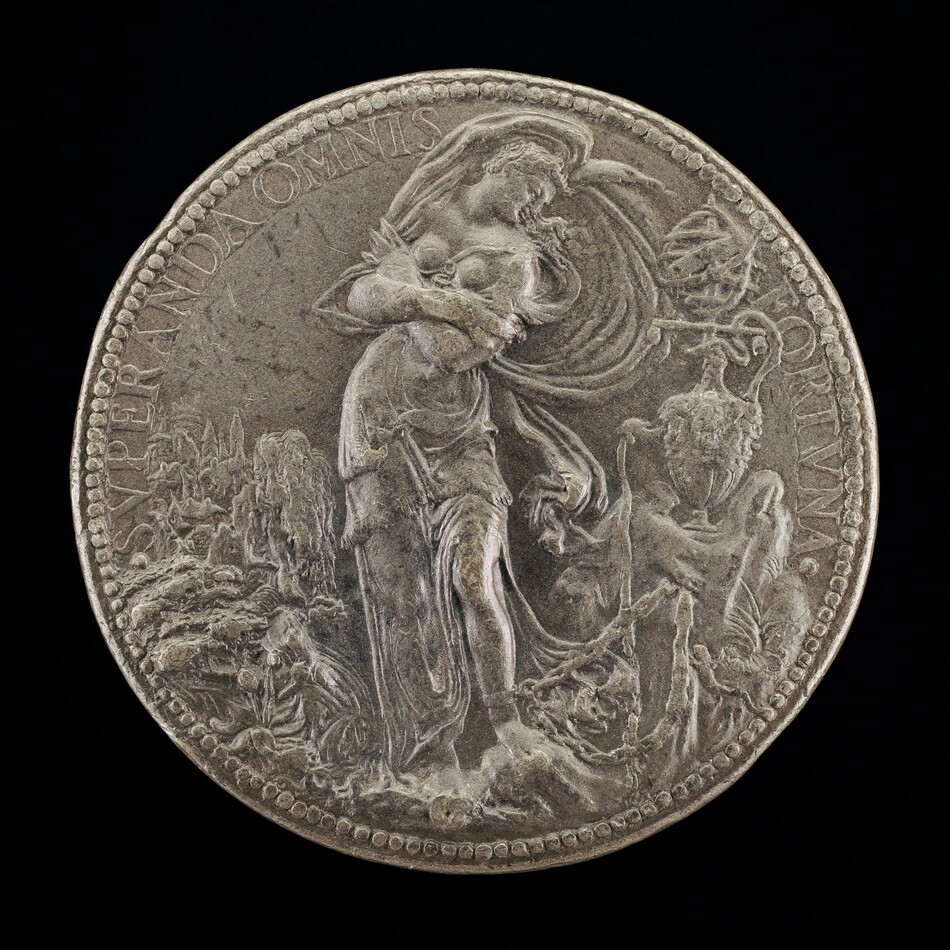 This is a photograph of a coin. The coin features a relief of a standing female figure draped in garments, next to symbolic elements. The background contains details such as trees and natural elements, as well as another figure to the right. The rim of the coin is inscribed with the words "SVPERANDA OMNIS" and "FORTVNA". The craftsmanship on the coin shows rich narrative or allegorical representation, with detailed depictions of clothing and surrounding elements.