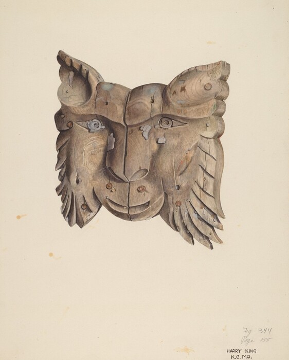 The sculpture is a wooden carving of a feline face. It is rendered in shades of brown wood with visible grain patterns and textures. The eyes and features of the face are intricately carved. The wood appears weathered with knots and imperfections. The carving includes detailed ears and a mane that fans out from the sides of the face. The artwork is mounted on a plain light-colored background.