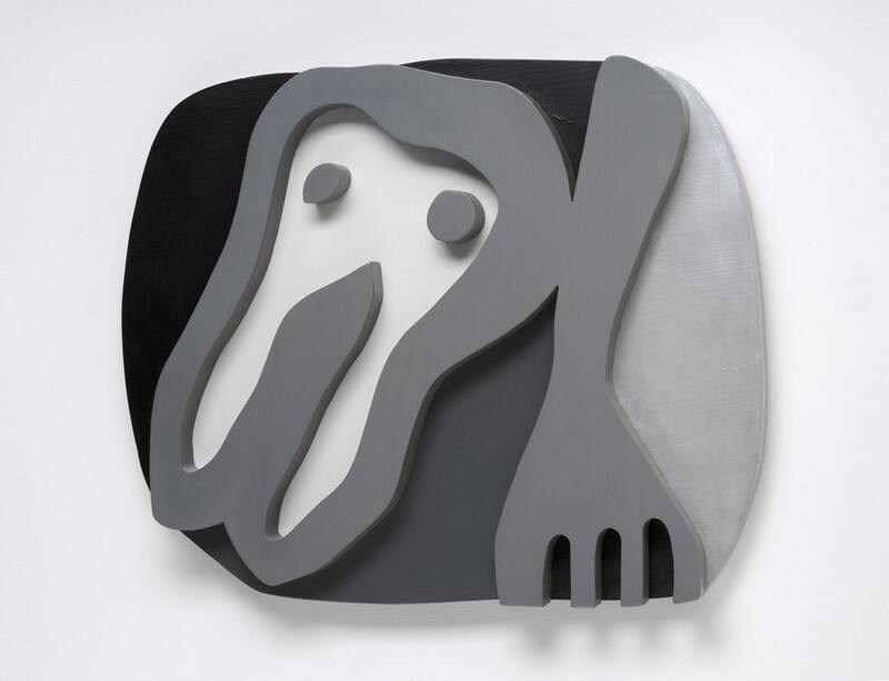 A cartoonish tooth-like form and a fork float against a roughly oval field in this abstracted wooden sculpture. Presumably the shirt front of the sculpture's title, the tooth-like form takes up the left half of the composition. It has a rounded top with two pointed root-like legs below, and has two dots like eyes near the top. The fork to our right points downward and the four tines are cut off by the bottom edge of the composition. The shirt front, dots, and fork are carved and painted nickel gray so they look like thick outlines in low relief. The background to our left and over the shirt front is black. The area between the shirt front and fork is dark gray, and the field to our right of the fork is silvery gray. The sculpture hangs on a white wall, and it casts a narrow shadow from the bottom edge.