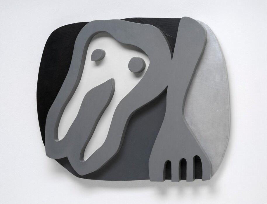 A cartoonish tooth-like form and a fork float against a roughly oval field in this abstracted wooden sculpture. Presumably the shirt front of the sculpture's title, the tooth-like form takes up the left half of the composition. It has a rounded top with two pointed root-like legs below, and has two dots like eyes near the top. The fork to our right points downward and the four tines are cut off by the bottom edge of the composition. The shirt front, dots, and fork are carved and painted nickel gray so they look like thick outlines in low relief. The background to our left and over the shirt front is black. The area between the shirt front and fork is dark gray, and the field to our right of the fork is silvery gray. The sculpture hangs on a white wall, and it casts a narrow shadow from the bottom edge.