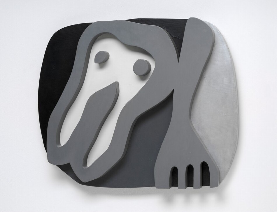A cartoonish tooth-like form and a fork float against a roughly oval field in this abstracted wooden sculpture. Presumably the shirt front of the sculpture's title, the tooth-like form takes up the left half of the composition. It has a rounded top with two pointed root-like legs below, and has two dots like eyes near the top. The fork to our right points downward and the four tines are cut off by the bottom edge of the composition. The shirt front, dots, and fork are carved and painted nickel gray so they look like thick outlines in low relief. The background to our left and over the shirt front is black. The area between the shirt front and fork is dark gray, and the field to our right of the fork is silvery gray. The sculpture hangs on a white wall, and it casts a narrow shadow from the bottom edge.