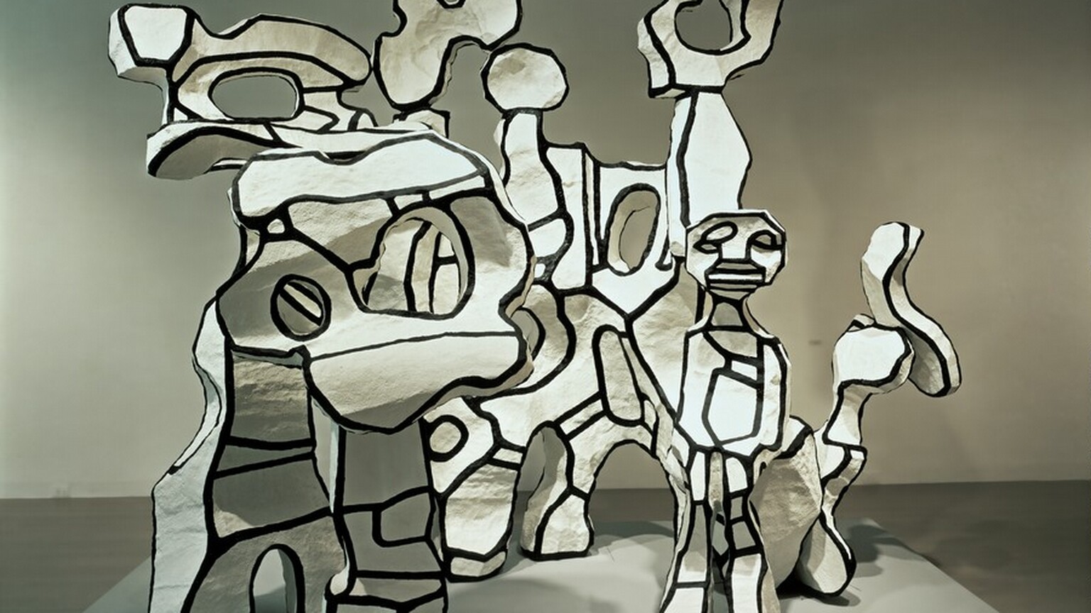 Abstract forms turn, twist, and curve up around a person with cartoon-like features in this free-standing sculptural piece.