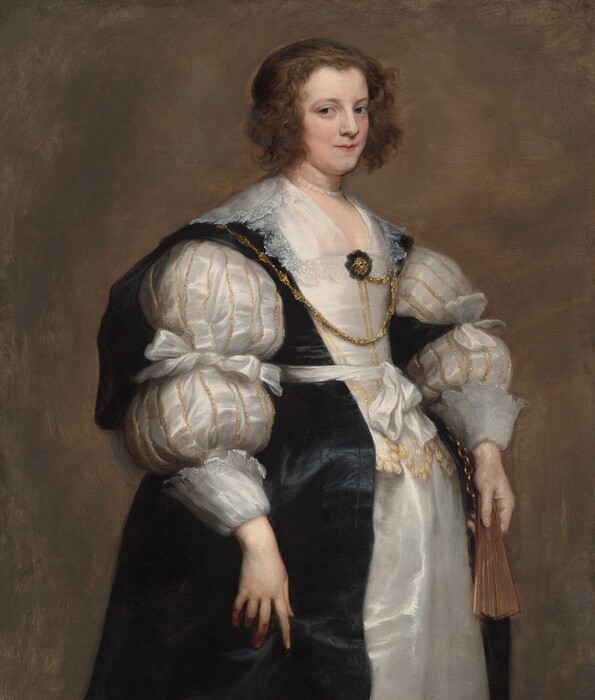 Shown from the knees up, a pale-skinned woman wearing a voluminous, gold-trimmed, white satin gown and a black overdress stands holding a closed fan in this vertical portrait painting. Her body and face are angled to our right, and she looks at us from the corners of her gray eyes. She has pale skin, a straight nose, thin lips, and a slight double chin. Chin-length brown waves frame her face, and the rest of her hair is pulled back. A pearl necklace lies at the base of her neck, though traces of another necklace, originally painted higher up on the neck like a choker, are visible. A lace-edged collar lies along her shoulders, and more lace lines a kerchief tucked into the low, straight neckline of her bodice. The gown’s puffy sleeves are tied around the elbows and end in wide lace-lined cuffs at the wrists. The sleeves and the front and bottom edges of the bodice are lined in glittery gold. A bejeweled gold brooch nestled in black lace is pinned to the front of her gown. A gold chain links the brooch to one side of the bodice before draping across her chest and lying over the other shoulder. A white satin ribbon is tied with a bow around her waist over the black overdress, which has subtle suggestions of a black-on-black pattern down the front. The fan is in her left hand, to our right, perhaps attached to a length of gold chain visible under her wrist. Her other hand rests in the folds of the black overdress. Some brushstrokes are visible in the woman’s clothing and in the walnut-brown background.