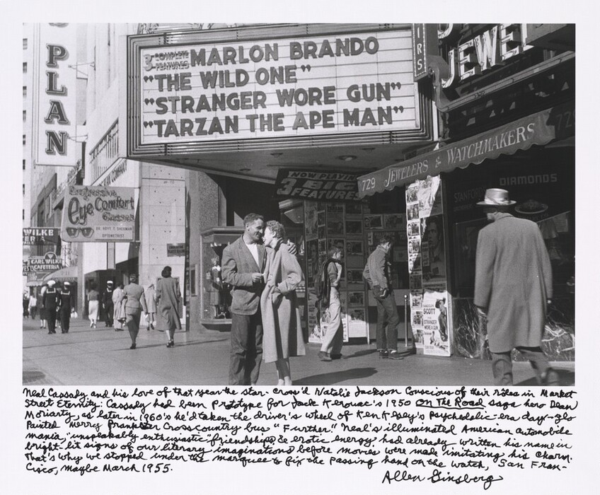 A young couple embrace under a movie theater marquee on a busy city street in this almost square black and white photograph. They are both pale-skinned with short, curly hair. The man is angled to our right while the woman faces him so we see her in profile. They both laugh as he holds her close with his left arm, on our right, draped across her shoulders. The man wears a white T-shirt under a loose blazer and baggy pants. The woman wears a loose-fitting, knee-length coat, and the hand we can see is in the pocket. The street stretches behind them and to our left, and people walk in both directions. The pedestrians wear similar clothing except for three sailors in the distance who stand out because of their white caps. Two young men stand near the couple examining the posters outside the theater, and a man in a coat and hat walks toward them from the right. Storefront signs extend from buildings lining the street, and a rolled-up awning close to us advertises a jewelry and watchmaking store. The marquee over their heads reads, “3 Complete Features: Marlon Brando, ‘The Wild One,’ ‘Stranger Wore Gun,’ and ‘Tarzan the Ape Man.’” The artist wrote a long caption in round cursive under the image. It reads, “Neal Cassady and his love of that year the star-cross'd Natalie Jackson conscious of their rôles in Market Street Eternity: Cassady had been prototype for Jack Kerouac's 1950 On the Road saga hero Dean Moriarty, as later in 1960's he'd taken the driver's wheel of Ken Kesey's psychedelic-era day-glo painted merry prankster crosscountry bus ‘Further.’ Neal's illuminated American automobile mania, ‘unspeakably enthusiastic’ friendship & erotic energy had already written his name in bright-lit signs of our literary imaginations before movies were made imitating his charm. That's why we stopped under the marquee to fix the passing hand on the watch, San Francisco, maybe March 1955. Allen Ginsberg.”