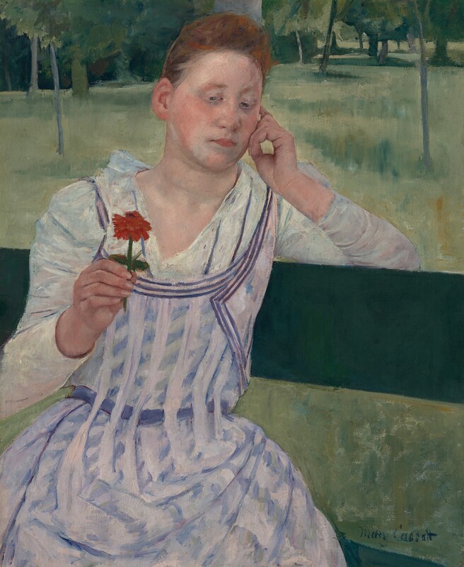 Shown from the knees up, a young woman with peachy skin and red hair sits facing us on a pine-green bench in this vertical painting. She sits with her body angled to our right, and her left elbow, on our right, hooks over the top slat of the bench. Her head tilts slightly to our right to rest on the curled fingers of that hand. In her other hand, she holds up a red flower on a short stem. Her hair is pulled up and back over a high forehead, and her cheeks are deeply flushed. Her pink lips are closed, and she looks down and to our left at the flower with gray eyes. She has an oval-shaped face and a hint of a double chin. Her white dress is painted with ice-blue shadows and folds. It has a deep V neck that reaches to an apron-like pinafore patterned with vertical bands of pale lilac that alternate with angled daubs of blue. Beyond her is a loosely painted landscape with grassy areas and clusters of tall trees painted in spring, emerald, and sea glass green. The edge of the grassy field nearly brushes the top edge of the canvas, and the trees are cropped by it. The artist signed the lower right, “Mary Cassatt.”