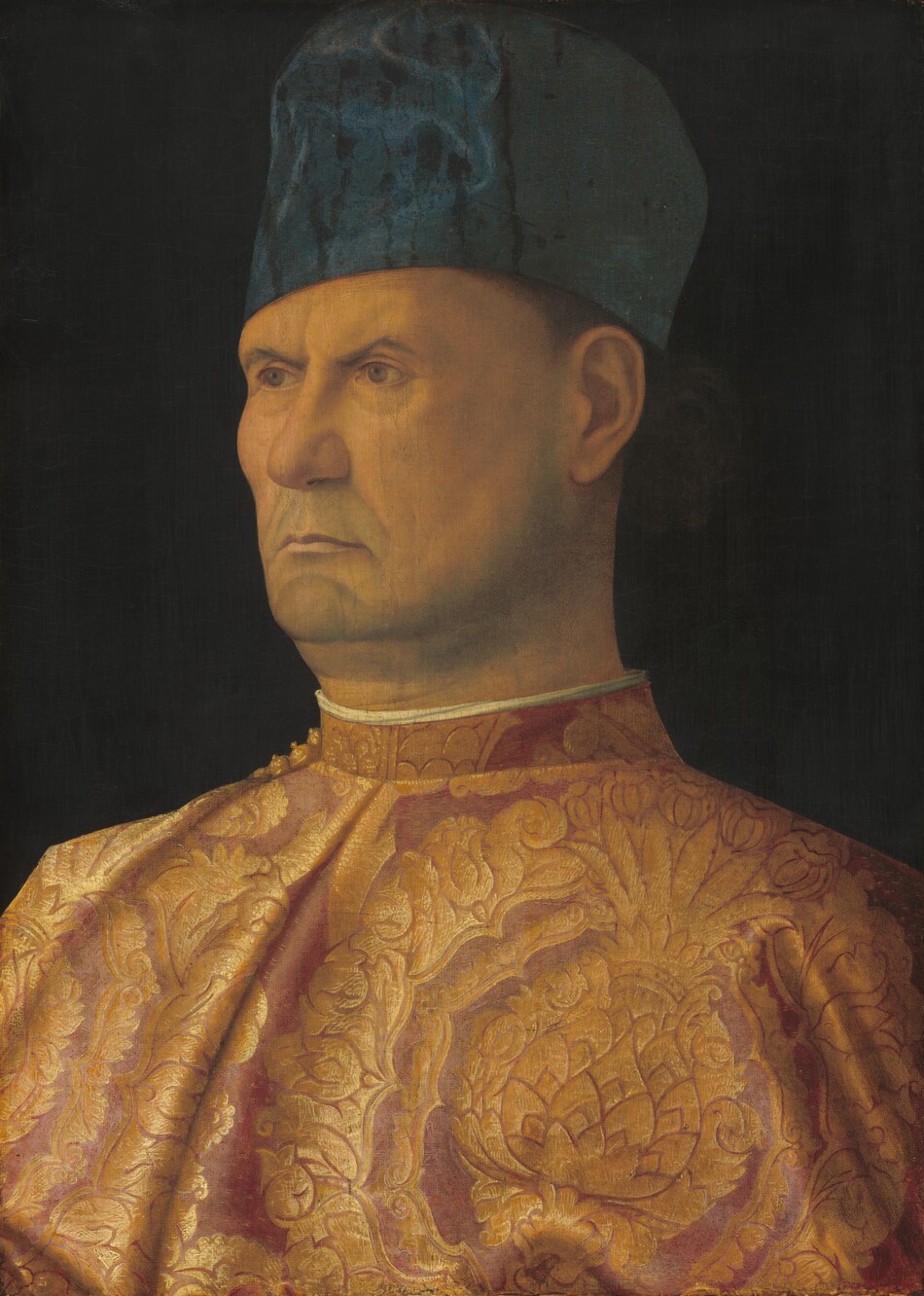 Shown from the chest up against a black background, a man with peachy skin wears a gold and rose-pink cloak in this vertical portrait painting. With his shoulders pulled back, the man’s body is angled to our left, and he looks in that direction with gray eyes under pointed, furrowed eyebrows. There are wrinkles around his eyes and mouth, and he has a five o-clock shadow along the jowls lining his jaw. He has a rounded nose, and the corners of his thin, pale pink lips turn downward. The hint of closely cropped, dark hair is seen around his ear under his tall, brimless, cobalt-blue cap. His cloak has a stylized floral pattern around pineapples in gold, against a dusky-rose pink background. The high neck of his cloak is lined with white.