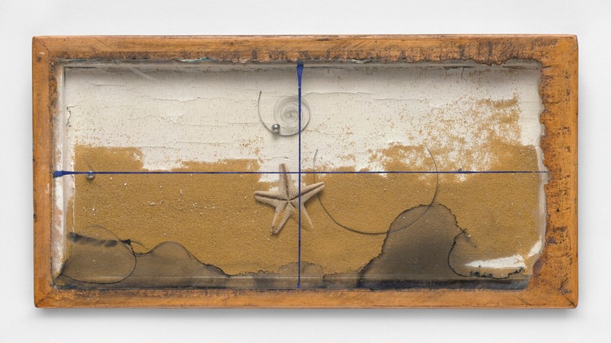 The image displays various shapes and lines in a wooden frame. A blue line intersects horizontally and vertically, dividing the piece into four sections. Inside the frame are textured layers in earthy tones resembling a sandy beach with a desert-like backdrop. A starfish and a shell are near the center. Lines and patches at the bottom suggest movement like waves.