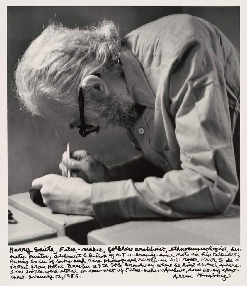 Harry Smith, Film-maker, folklore archivist, ethnomusicologist, hermetic painter, alchemist & Bishop of O.T.O. erasing some note in his calendar, Packing boxes of books and rare phonograph records in his room prior to departure from Hotel Breslin 28th St. & Broadway where he lived several years. Some boxes were stored in basement of Film-Maker's Archive, some at my apartment. January 12, 1985.