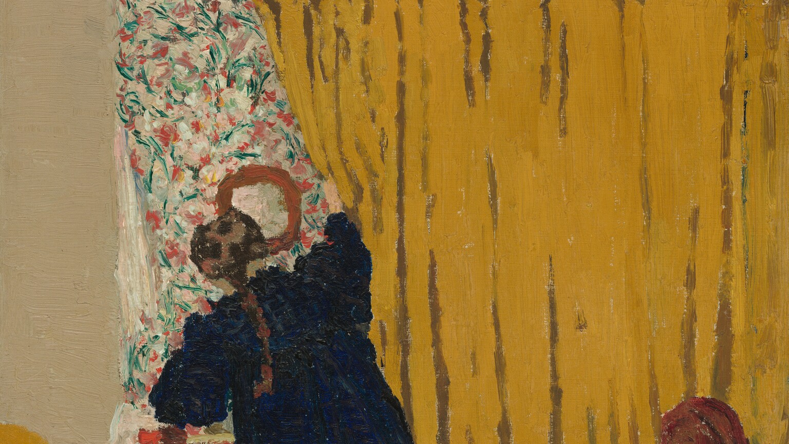 A woman pushes aside a deep golden yellow curtain that fills three-quarters of this nearly square painting. The curtain runs on a rod parallel and close to the top of the canvas, extends off the right edge, and falls behind a bed covered in the same color. The bed is cropped by the bottom and left edges of the painting, and a brown, arched wood footboard almost reaches the right side. The woman stands on the far side of the bed, facing away from us as she pulls at the curtain with her right hand. She wears a navy-blue dress and a brown braid falls down her back. She reveals an area covered in a pink, green, and white floral pattern that seems to match the size of the curtain, at least along the left edge where it is exposed. A round mirror hangs on the floral-patterned area above a red piece of furniture, perhaps a small table or stool. The wall around the patterned area and curtain is painted bone white. A line incised in the paint running from the top left corner of the floral area to the top edge of the canvas suggests a crack in the wall. The paint is loosely applied so brushstrokes are visible throughout, especially in the floral pattern. The artist’s signature is painted in red in the lower left corner: "E. Vuillard."