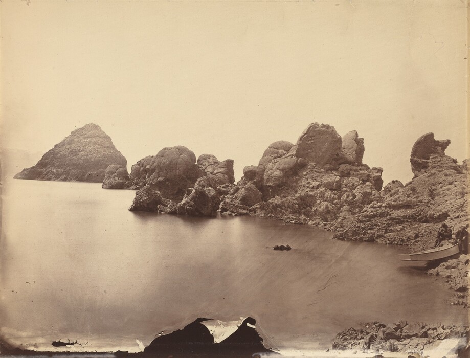 The image displays a coastal landscape with a calm body of water, a rocky shoreline, a rocky hill in the distance, and several people near a boat. The sky is a soft sepia tone, and the scene has a monochromatic palette emphasizing textures.