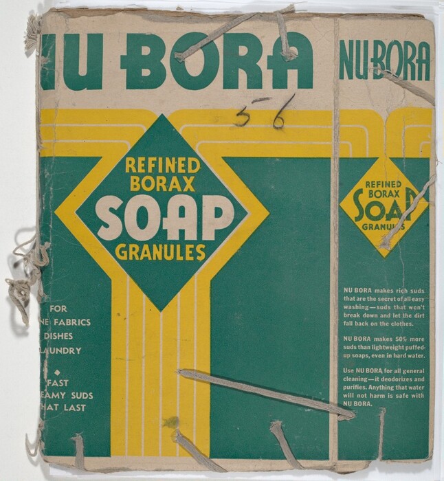 This is a photograph of a vintage soap packaging. The packaging displays the branding "NU BORA" in large text at the top, and prominently features the product description "REFINED BORAX SOAP GRANULES" within a green diamond shape, bordered by yellow lines. Additional text on the left and right sides describes the product's applications, such as "FOR FINE FABRICS, DISHES, LAUNDRY" and promotional information about its cleaning effectiveness and properties. The colors used are mainly green, yellow, and white, and the overall condition of the package shows signs of wear and tear, with some strings and stitching visible on the left side.