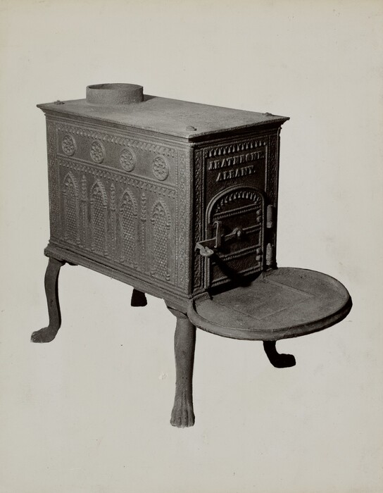 The image displays a cast iron stove featuring intricate decorative details. The stove is made of dark grey iron, with circle and arch patterns on its sides, a rectangular door inscribed with "Rathbone Albany", and is elevated on three paw-shaped legs. The stove has a round disklike surface on its front, emphasizing its functional design.