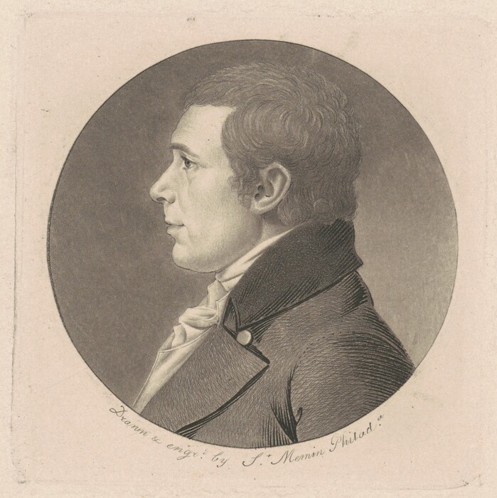 The image shows a man's head-and-shoulders profile facing left. He has defined, classically handsome features, short curly hair, and is wearing a high-collared coat with a visible cravat or ascot. The background is a plain, light-toned surface, emphasizing the man in the central circle.