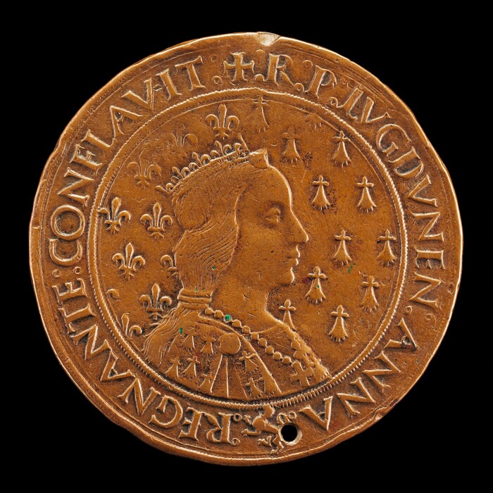 The image displays a round, coin-like sculpture depicting a portrait of a woman with a crown and regal attire. The material appears to be metallic with a brownish hue. The profile features detailed facial characteristics and a complex hairstyle. Inscriptions in capital letters surround the portrait, with decorative elements filling the background space. The sculpture shows fine detail and craftsmanship, with a small hole near the bottom edge.