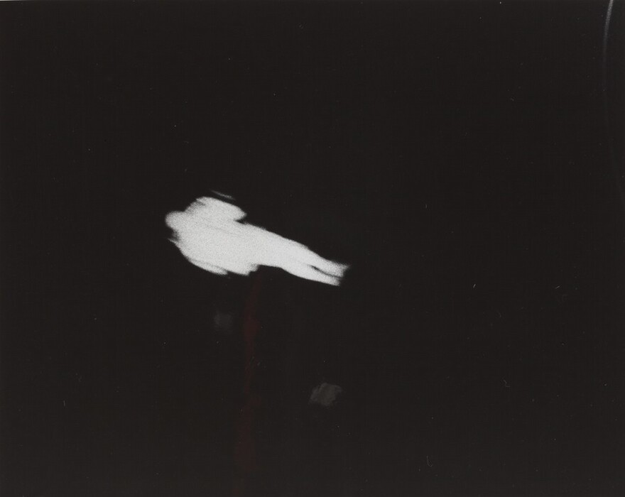 The image features a white silhouette shape against a black background, forming an abstract figure resembling an astronaut floating in space. The shape suggests a helmet on one end and arms and legs extending outwards. The abstract representation allows for connections to space exploration or a celestial journey, reimagining traditional forms in a minimalist style.